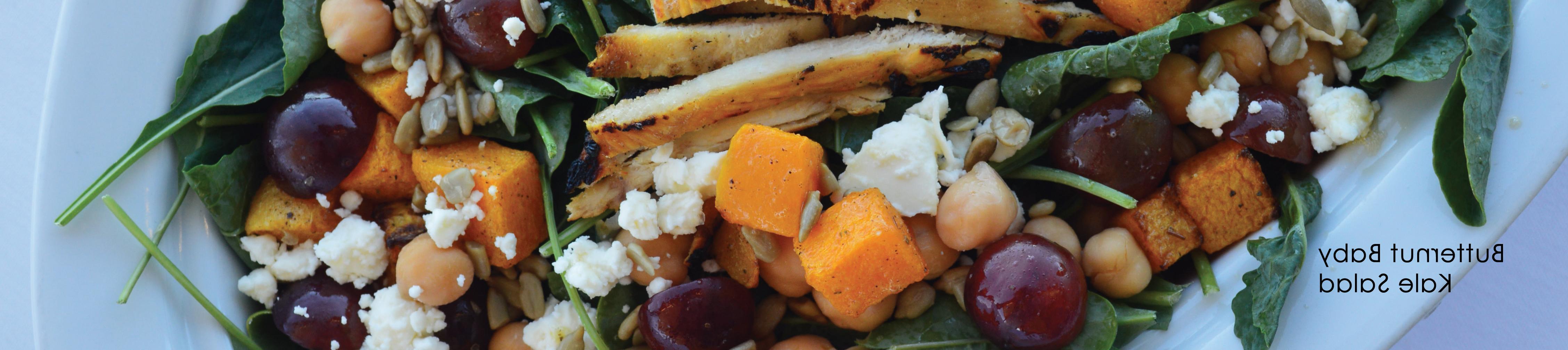 Butternut Baby Kale Salad. Nice salad plate with greens, croutons, grapes, cheese, and chicken on white plate.